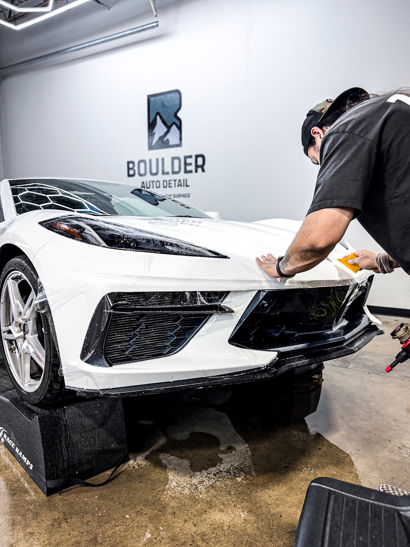 Detailer squeegeeing paint protection film onto the front bumper of a white Corvette